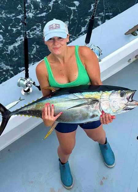 Pretty young lady holds out the nice yellowfin tuna she caught.